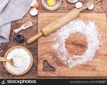square wooden kitchen board with rolling pin and wheat flour in a wooden bowl, top view