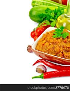 Squash paste in a clay bowl, hot peppers, tomatoes, zucchini, parsley, oil, garlic isolated on white background