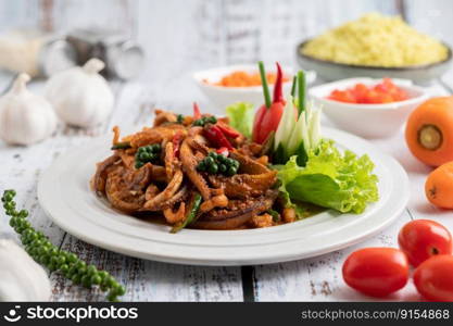 Squid fried with curry paste in white plate, with vegetables and side dishes on a white wooden floor. Selective focus.