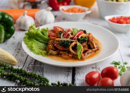 Squid fried with curry paste in white plate, with vegetables and side dishes on a white wooden floor. Selective focus.