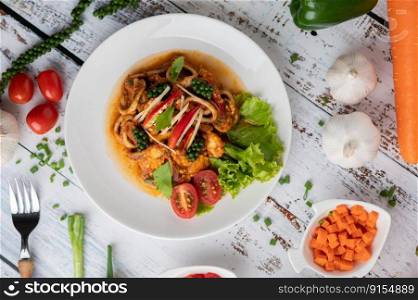 Squid fried with curry paste in white plate, with vegetables and side dishes on a white wooden floor. Top view.