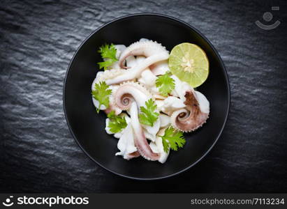 squid salad bowl with lime herbs and spices on black background top view / Tentacles octopus cooked appetizer food seafood cooked in the restaurant