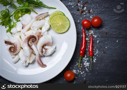 squid salad with lemon herbs and spices on dark background top view / Tentacles octopus cooked appetizer food hot and spicy chilli sauce seafood cooked served on plate in the restaurant