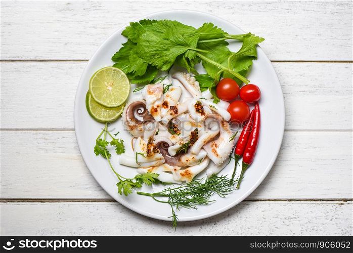 squid salad with lemon herbs and spices on wooden background top view / Tentacles octopus cooked appetizer food hot and spicy chilli sauce seafood cooked served on white plate in the restaurant