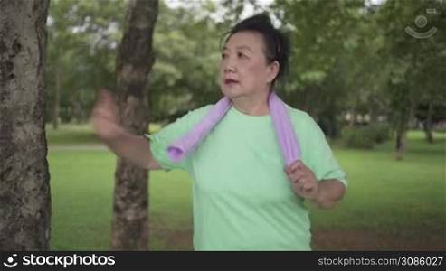 Sr Exercise 48Asian senior woman running and exercising at the park, standing next to the tree and rest, human body wellness, female health care, life insurance plan, work out routine, good health for better life