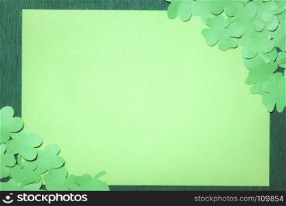 St Patrick banner concept with many paper clovers in two opposite corners of a blank paper, centered on a dark green wooden background.