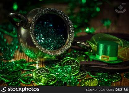 St.Patrick&rsquo;s day holiday symbol. Shamrocks, coins, leprechaun hat and antique silver pot on an old rustic wood background. Close up view. Selective focus. Bokeh.