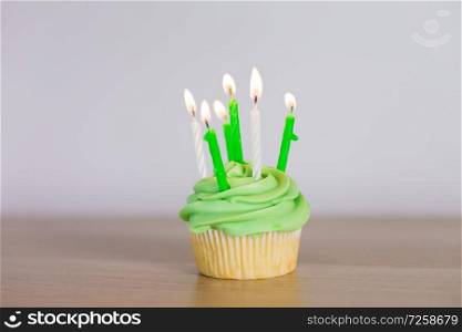 st patricks day, birthday, holidays and celebration concept - green cupcake with six burning candles on table. green cupcake with six burning candles on table
