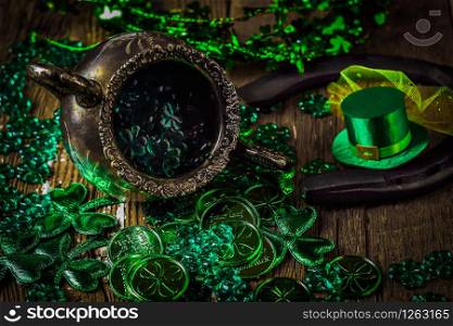St. Patricks Day composition. Shamrocks, horseshoe, coins, leprechaun hat and silver pot on vintage style wood background. Close up view. Selective focus. Bokeh.