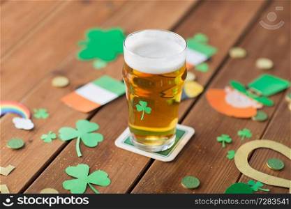 st patricks day, holidays and celebration concept - glass of draft light beer, shamrock, gold coins and other party props on wooden table. glass of beer and st patricks day party props