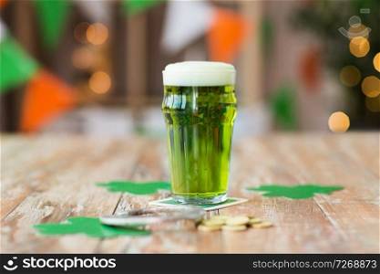 st patricks day, holidays and celebration concept - glass of green beer with horseshoe, shamrock and gold coins on wooden table. glass of green beer, horseshoe and golden coins