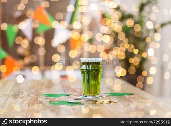 st patricks day, holidays and celebration concept - glass of green beer with horseshoe, shamrock and gold coins on wooden table. glass of green beer, horseshoe and golden coins