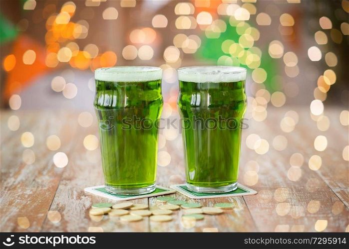 st patricks day, holidays and celebration concept - glasses of green beer and gold coins on wooden table. glasses of green beer and gold coins on table
