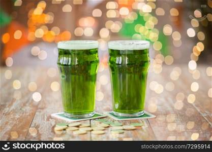 st patricks day, holidays and celebration concept - glasses of green beer and gold coins on wooden table. glasses of green beer and gold coins on table