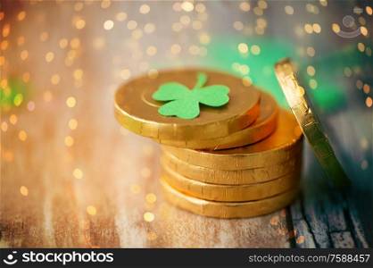 st patricks day, holidays and celebration concept - gold coins with shamrock on wooden table over festive lights. gold coins with shamrock on wooden table