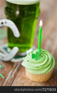 st patricks day, holidays and celebration concept - green cupcake with candle, glass of beer and horseshoe on wooden table. green cupcake with candle, beer and horseshoe