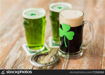 st patricks day, holidays and celebration concept - shamrock on glasses of beer and horseshoe on wooden table. shamrock on glass of beer and horseshoe on table