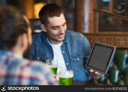 st patricks day, leisure and technology concept - happy male friends with tablet pc computer drinking green beer at bar or pub. friends with tablet pc and green beer at pub