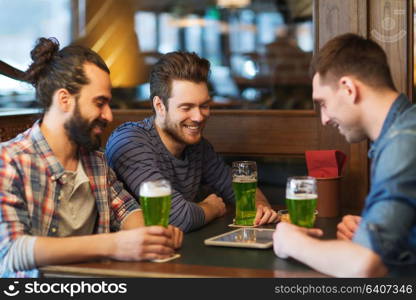 st patricks day, leisure and technology concept - happy male friends with tablet pc computer drinking green beer at bar or pub. friends with tablet pc and green beer at pub
