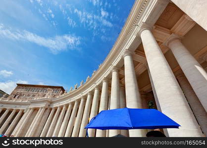 St. Peter’s Basilica colonnades in Vatican City. Blue umbrella held by a tourist harmonizes with sky.. St. Peter’s Basilica colonnades in Vatican City. Blue umbrella harmonizes with sky