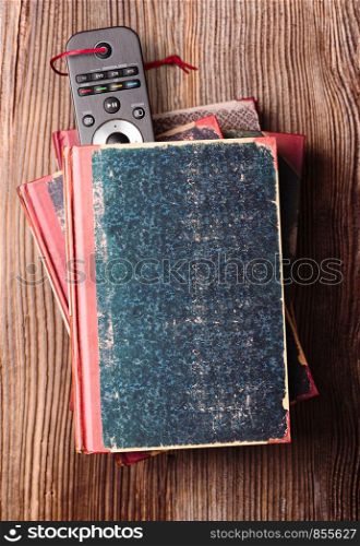 Stack a few books on wooden table with bookmark in shape of tv remote inserted in one book