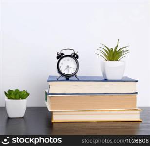 stack books on a black table, on top a ceramic pot with a green plant, concept of back to school
