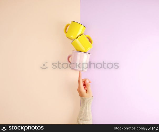 stack ceramic cups are supported by a female hand on a beige lilac background, copy space