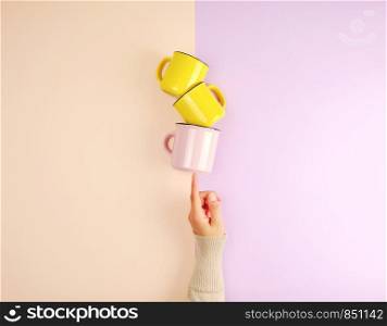 stack ceramic cups are supported by a female hand on a beige lilac background, copy space