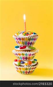 stack decorative cup cakes with burning candle yellow background