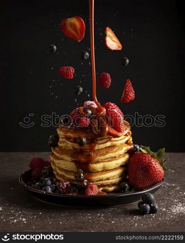 Stack of american pancakes with levitating berries and falling caramel  cajeta . Creative levitation photography.