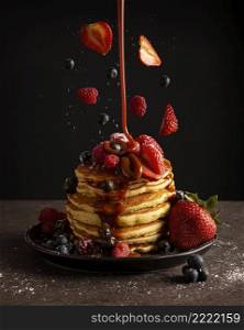 Stack of american pancakes with levitating berries and falling caramel (cajeta). Creative levitation photography.