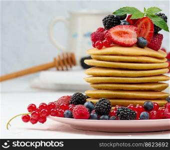 Stack of baked pancakes with fruits in a round plate on a white table, delicious breakfast
