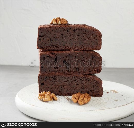 stack of baked pieces of brownie chocolate cake with nuts on a wooden board, delicious dessert