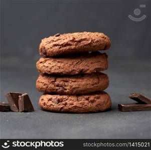 stack of baked round chocolate chip cookies and pieces of chocolate on a black table, close up