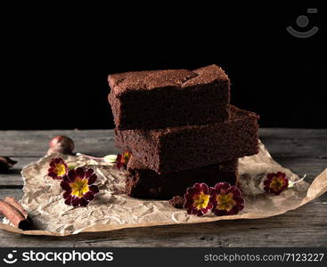 stack of baked square pieces of chocolate brownie cake on brown parchment paper, black background