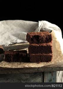 stack of baked square pieces of chocolate brownie cake on brown parchment paper, black background