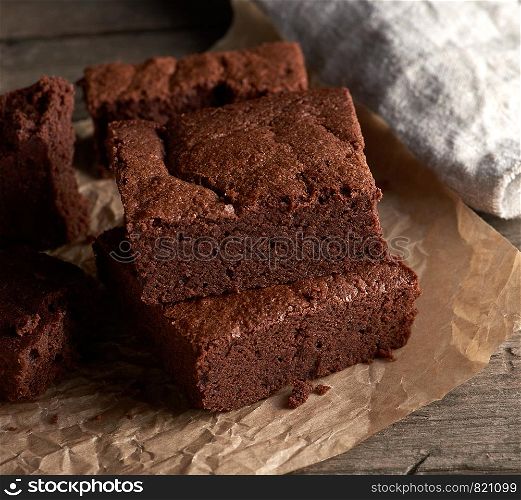 stack of baked square pieces of chocolate brownie cake on brown parchment paper, top view