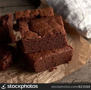 stack of baked square pieces of chocolate brownie cake on brown parchment paper, top view