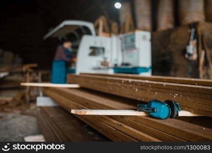 Stack of boards, carpenter in uniform at woodworking machine on background, lumber industry, carpentry. Wood processing on factory, forest sawing in lumberyard, sawmill. Stack of boards, carpenter at woodworking machine