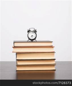 stack of books and a black alarm clock on the table, white background, copy space