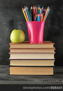 stack of books and a blue stationery glass with multi-colored wooden pencils, back to school concept