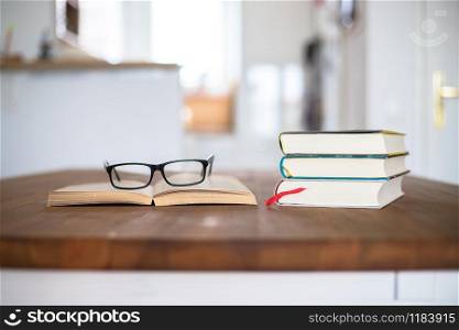Stack of books and glasses lying on wooden desk at home. Knowledge and science