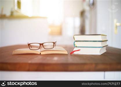 Stack of books and glasses lying on wooden desk at home. Knowledge and science