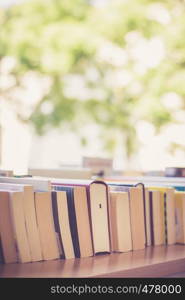 Stack of books, blurry background: Charity book flea market, outdoors. Text space.