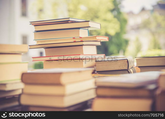 Stack of books, blurry background: Charity book flea market, outdoors. Text space.