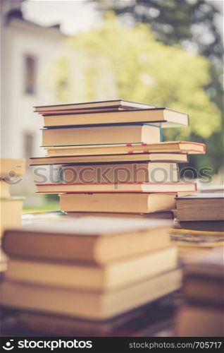 Stack of books, blurry background: Charity book flea market, outdoors. Text space.