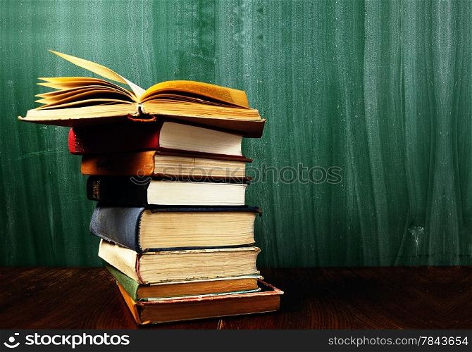 stack of books in front of blank green blackboard .Warm tones.