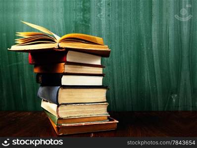 stack of books in front of blank green blackboard .Warm tones.