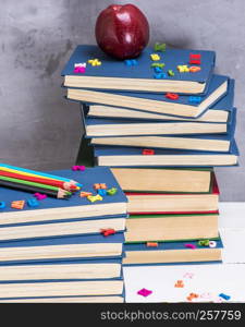 stack of books in the blue cover, multicolored wooden pencils and a red apple