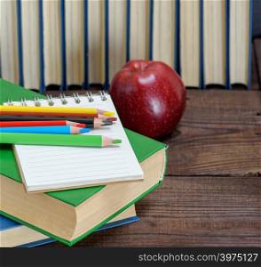 stack of books in the blue cover, multicolored wooden pencils and a red apple